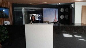 A reception desk with a large screen displaying an image of the Eiffel Tower, a clock, and a plant. - Hotel Eiffel (Ensenada)