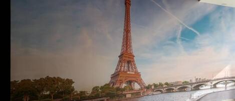 A mural of the Eiffel Tower with a river and bridge in the foreground.