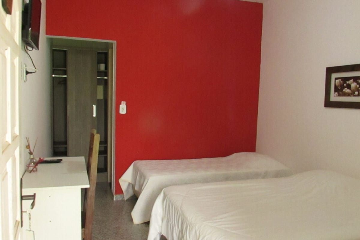 A room with two beds, a desk, and a red wall.