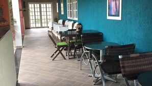 Un espacio de estar al aire libre techado con una mesa, sillas, un sofá y un televisor montado en la pared.
