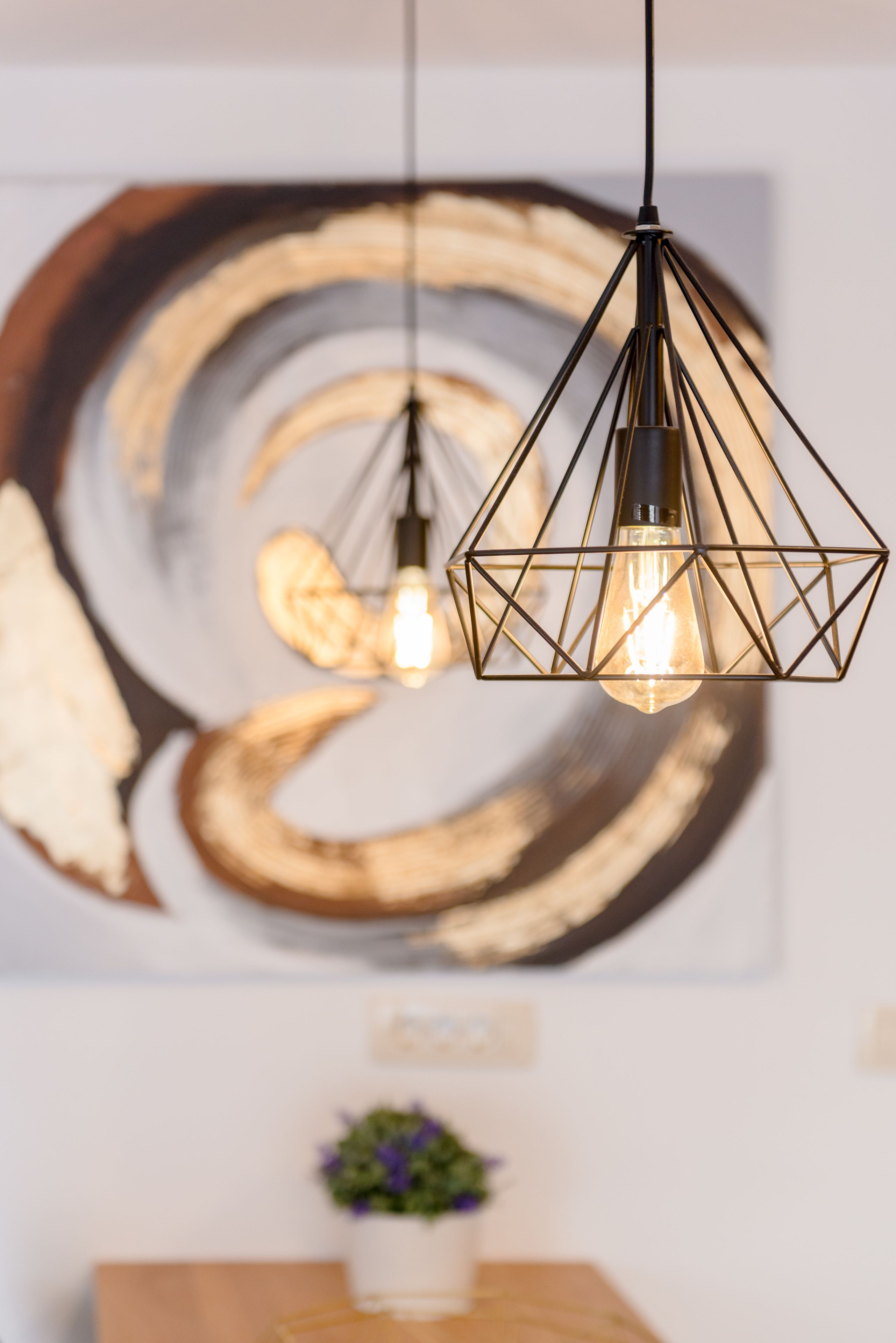A geometric pendant light fixture with a visible filament bulb, hanging from a black cord.