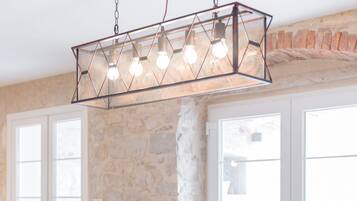 A dining area with a long wooden table, six chairs, a fruit bowl, and a hanging light fixture.