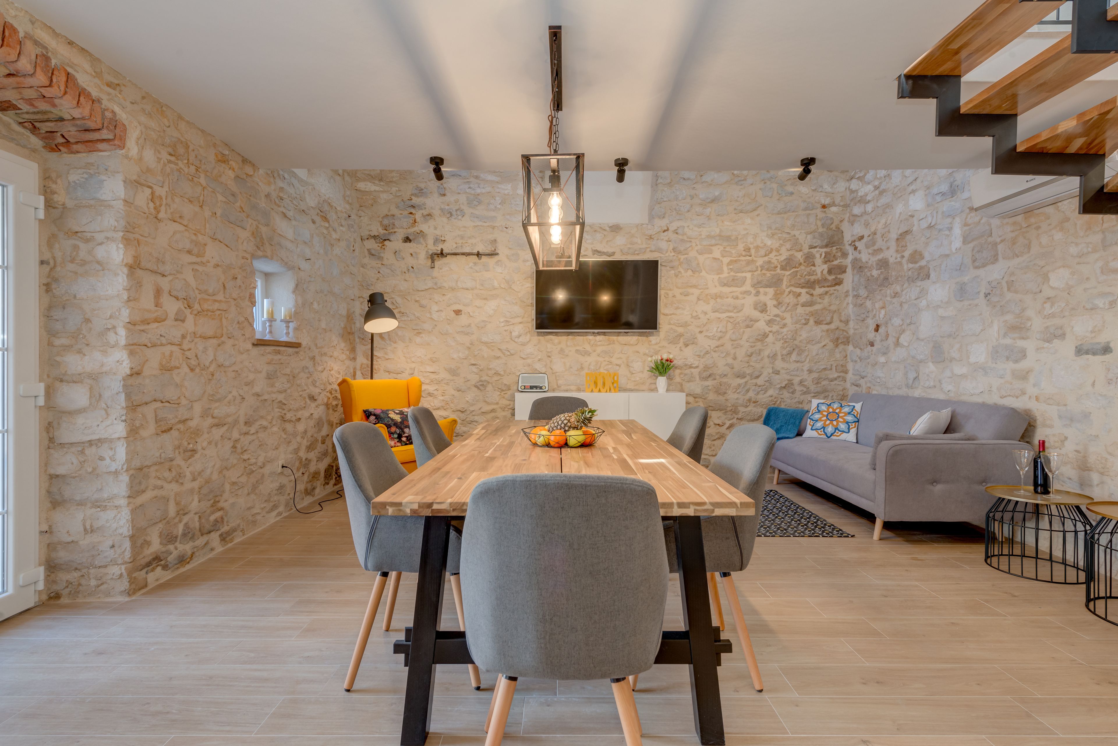A dining area with a wooden table, grey chairs, and a stone wall.