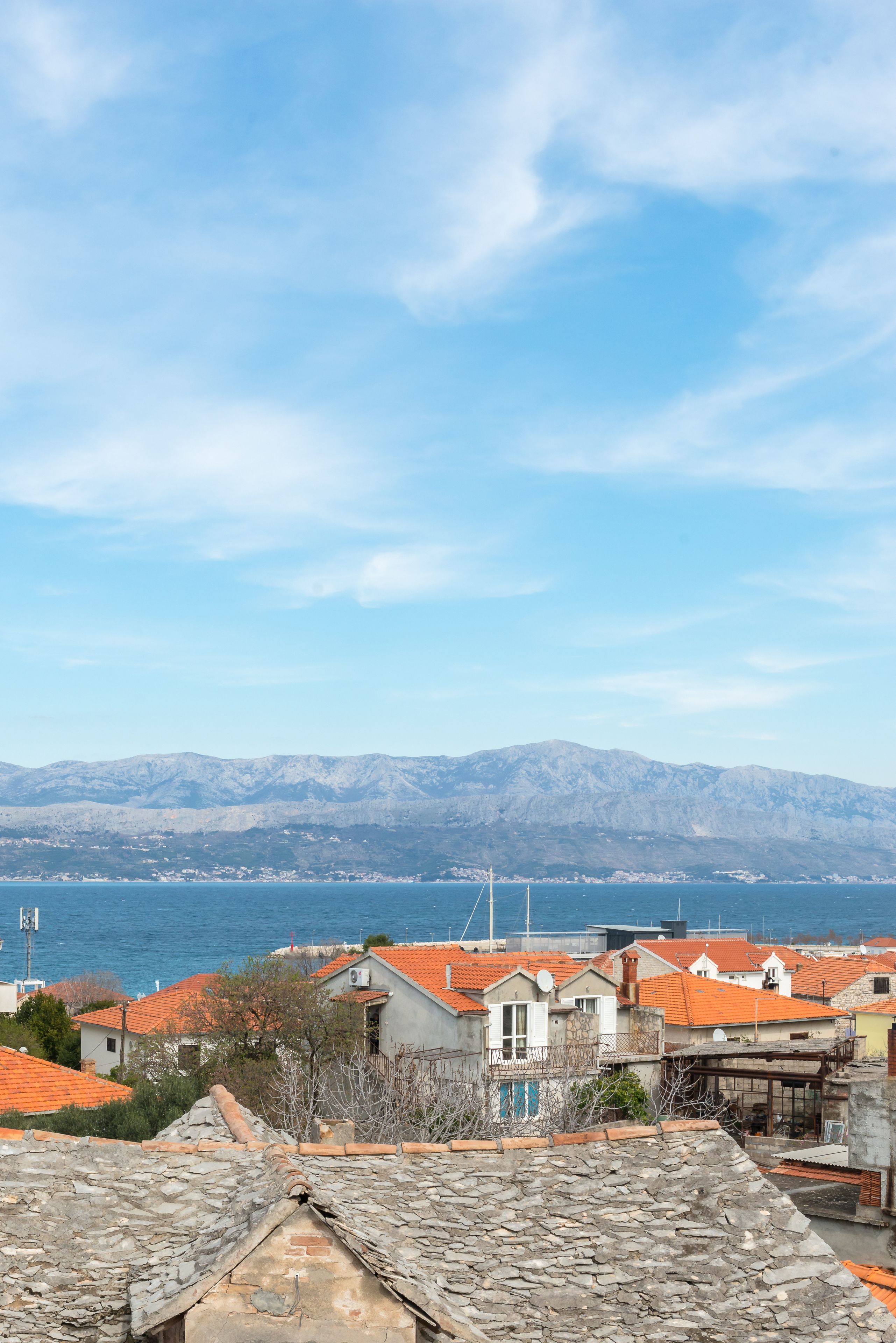 A coastal town with stone buildings and a view of the sea and mountains.