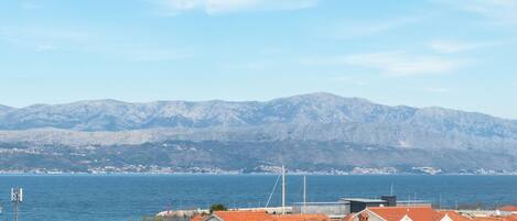 A coastal town with stone buildings and a view of the sea and mountains.