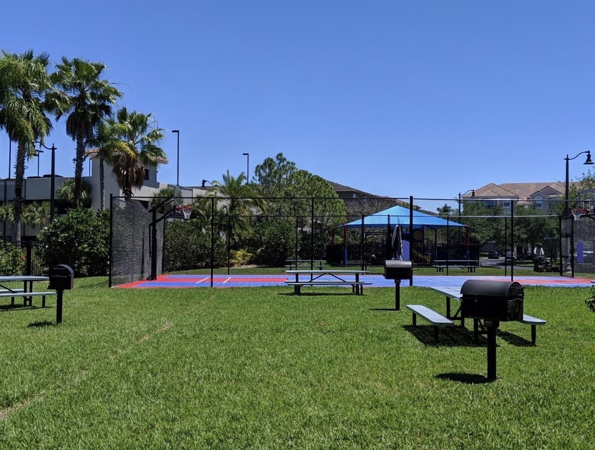 A park with picnic tables, a basketball court, and a covered area.