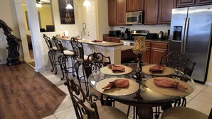 A modern kitchen with stainless steel appliances, a dining area with a round glass table, and dark wood chairs. - Executive 3 Br Villa @Universal / Vista Cay/Conv.Center (Orlando)