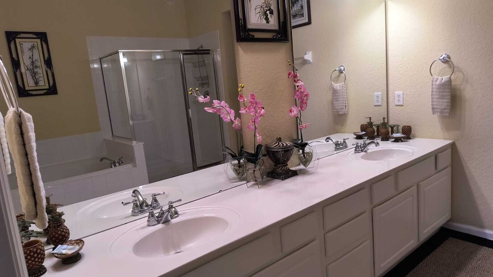 A long bathroom with two sinks, a large mirror, and a shower.