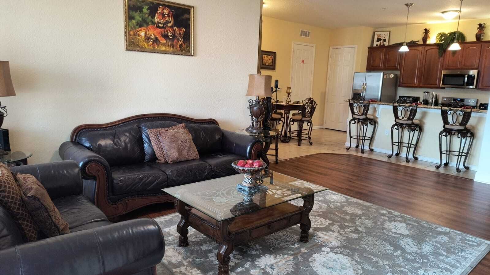 A living room with a dark leather sofa, a glass coffee table, and a dining area with a chandelier.