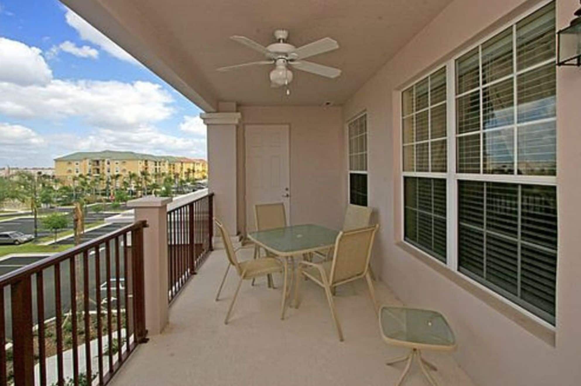 A balcony with a table and chairs, a ceiling fan, and a view of a building and palm trees.