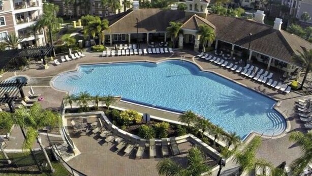 A large swimming pool surrounded by lounge chairs and palm trees, with multi-story buildings in the background. - Executive 3 Br Villa @Universal / Vista Cay/Conv.Center (Orlando)