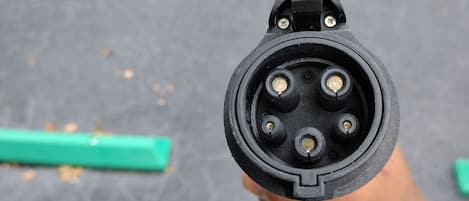 Gros plan d'une prise électrique noire à quatre broches, tenue dans une main.
