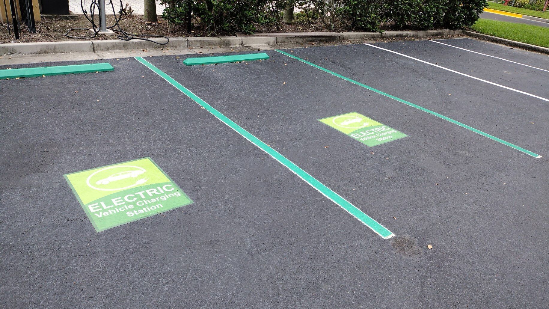 Ein Parkplatz mit Ladestationen für Elektrofahrzeuge, gekennzeichnet durch grüne Linien und Schilder.
