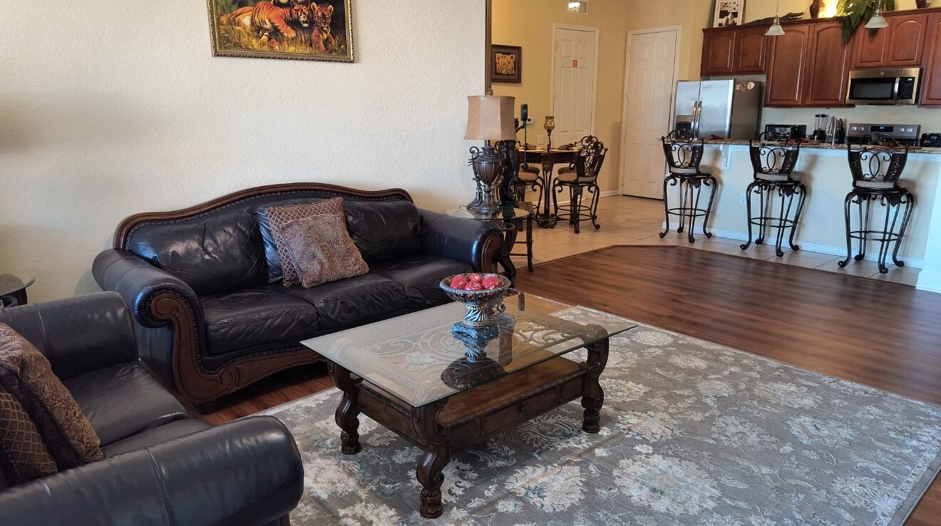 A living room with a black leather sofa, a glass coffee table, and a patterned rug.