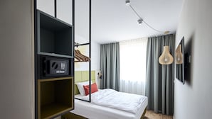 A modern hotel room with a bed, a green storage unit, a microwave, and a window with curtains. - Best Western Hotel Viernheim Mannheim (Viernheim)