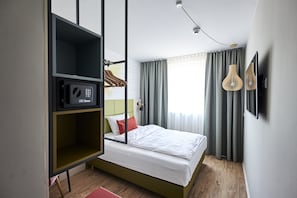 A modern hotel room with a bed, a green storage unit, a microwave, and a window with curtains. - Best Western Hotel Viernheim Mannheim (Viernheim)