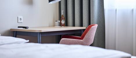 A hotel room with a desk, chair, lamp, and a bottle of water.