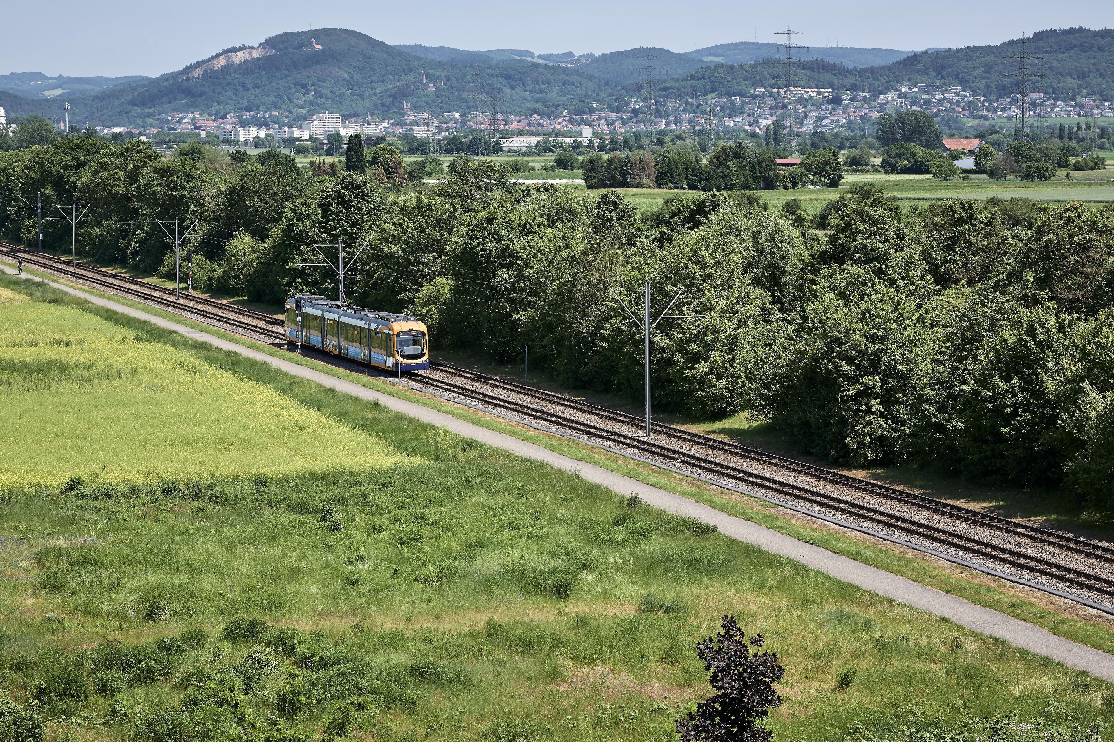 A train on a railway track with a green landscape and a town in the background.