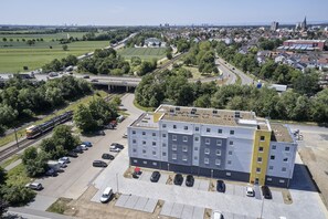 A multi-story building with a parking lot in front, surrounded by greenery and a railway line. - Best Western Hotel Viernheim Mannheim (Viernheim)