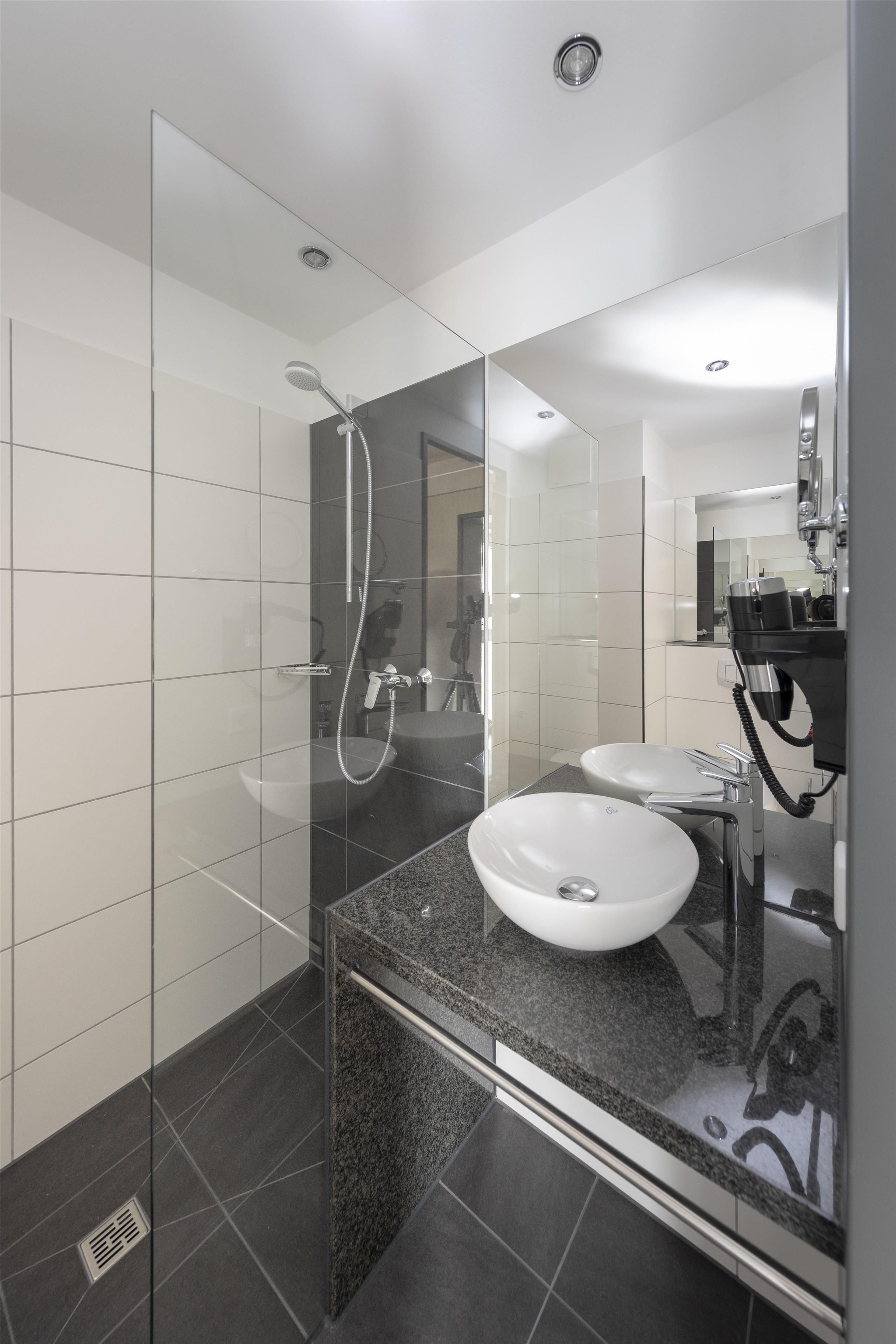 Une salle de bain moderne avec une douche à parois de verre, deux lavabos et un grand miroir.