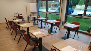 Un aula con pupitres de madera y sillas rojas, ventanas amplias y una pizarra.