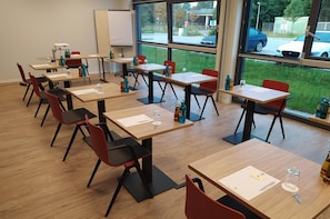 Un aula con pupitres de madera y sillas rojas, ventanas amplias y una pizarra.