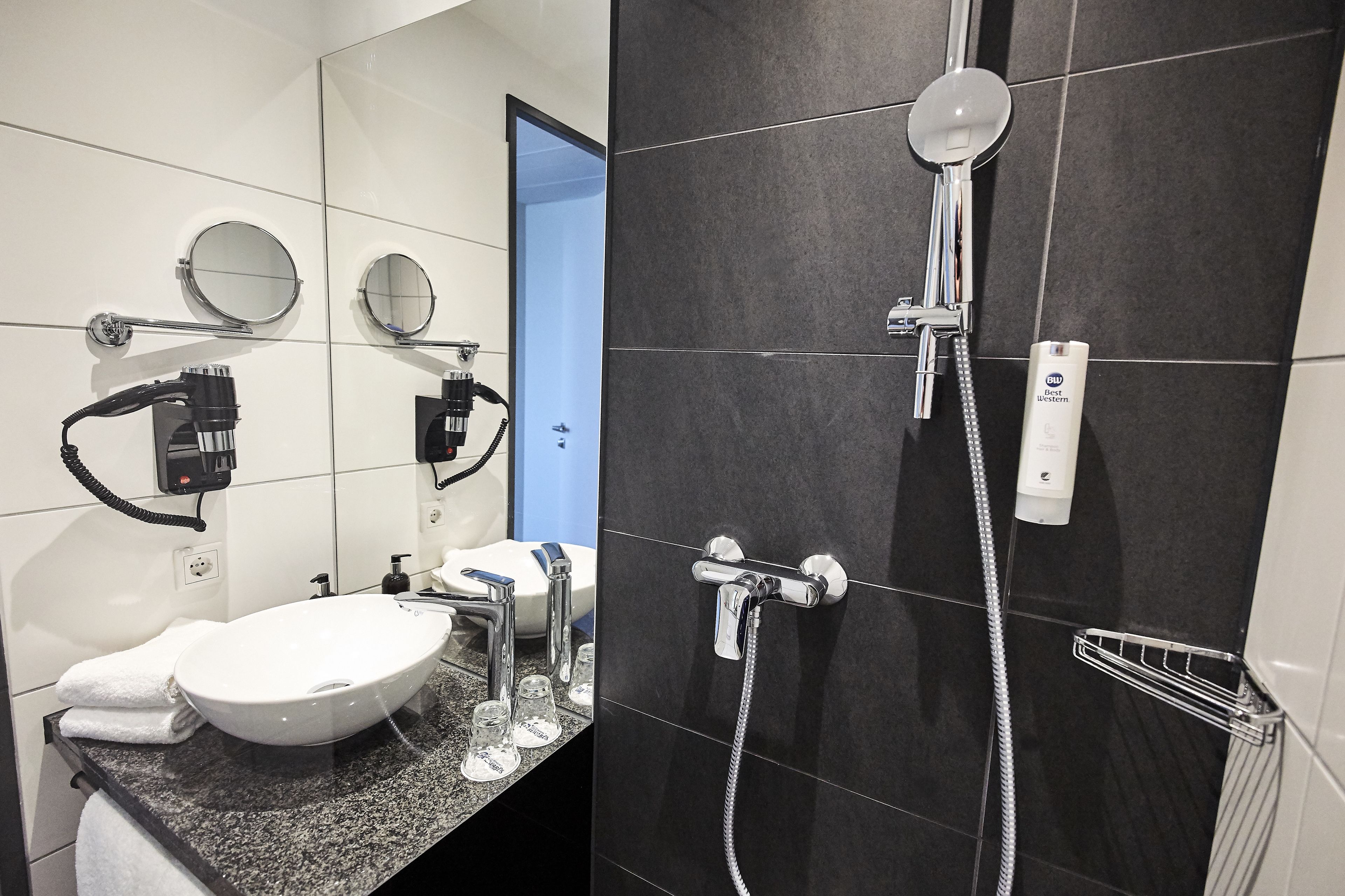 A modern bathroom with a white sink, two round mirrors, a handheld showerhead, and a handheld hairdryer.