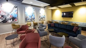 Un moderno espacio de descanso con diversas opciones de asientos, incluyendo sofás y sillones, un televisor de pantalla plana en la pared y arte abstracto en las paredes.