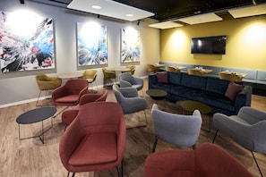 Un moderno espacio de descanso con diversas opciones de asientos, incluyendo sofás y sillones, un televisor de pantalla plana en la pared y arte abstracto en las paredes.