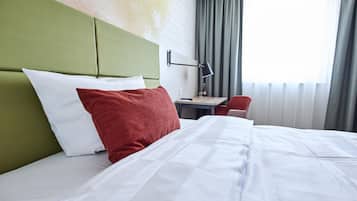 Una habitación de hotel con una cama, un escritorio, una silla y un ventanal con cortinas.