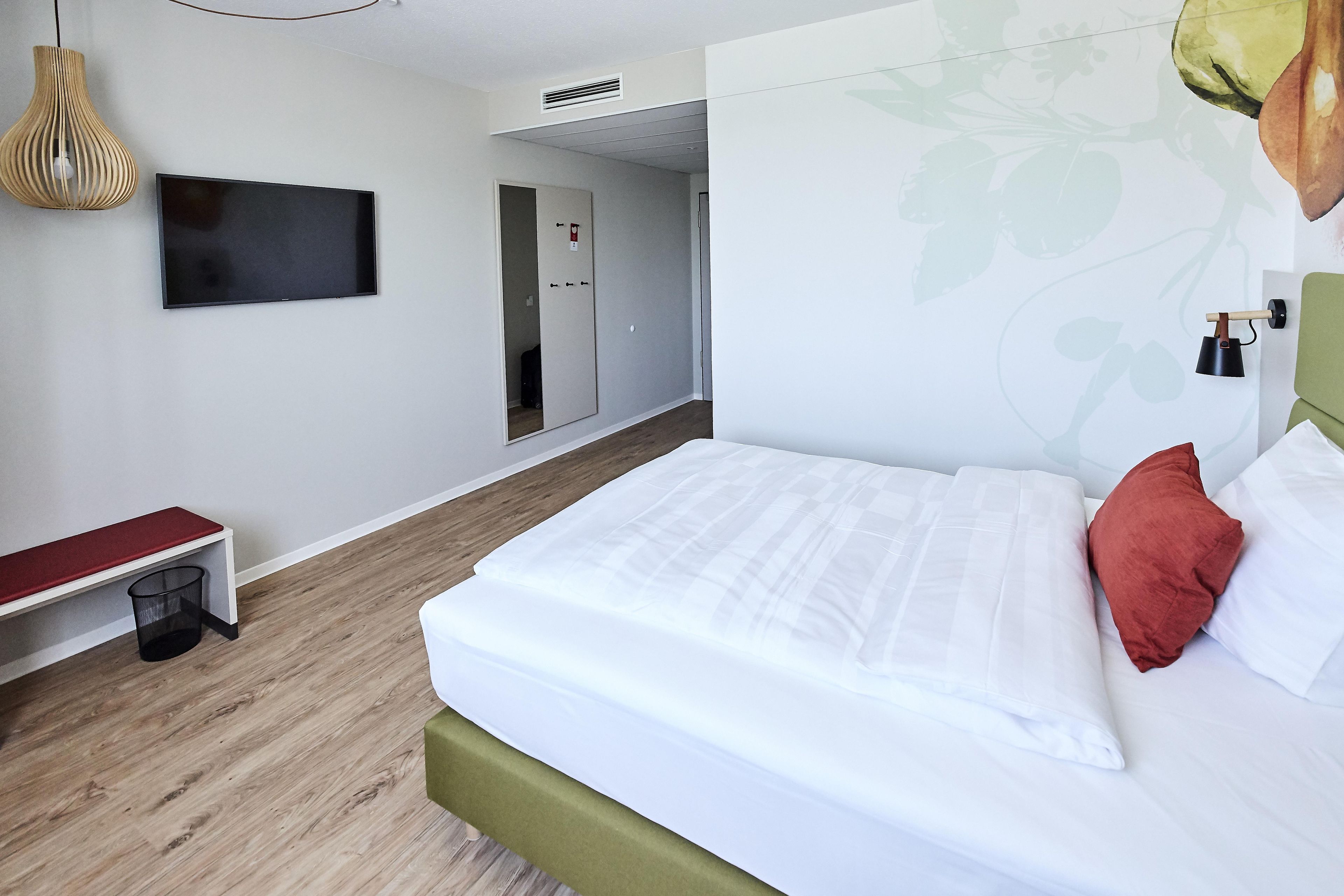 Ein Hotelzimmer mit einem Bett, einem Fernseher, einem Kleiderschrank und einer kleinen Bank.