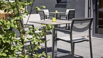 An outdoor seating area with tables and chairs, a bottle on one table, and a building in the background.