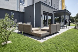 Un área de estar moderna al aire libre con mobiliario de mimbre y cerramiento de vidrio.