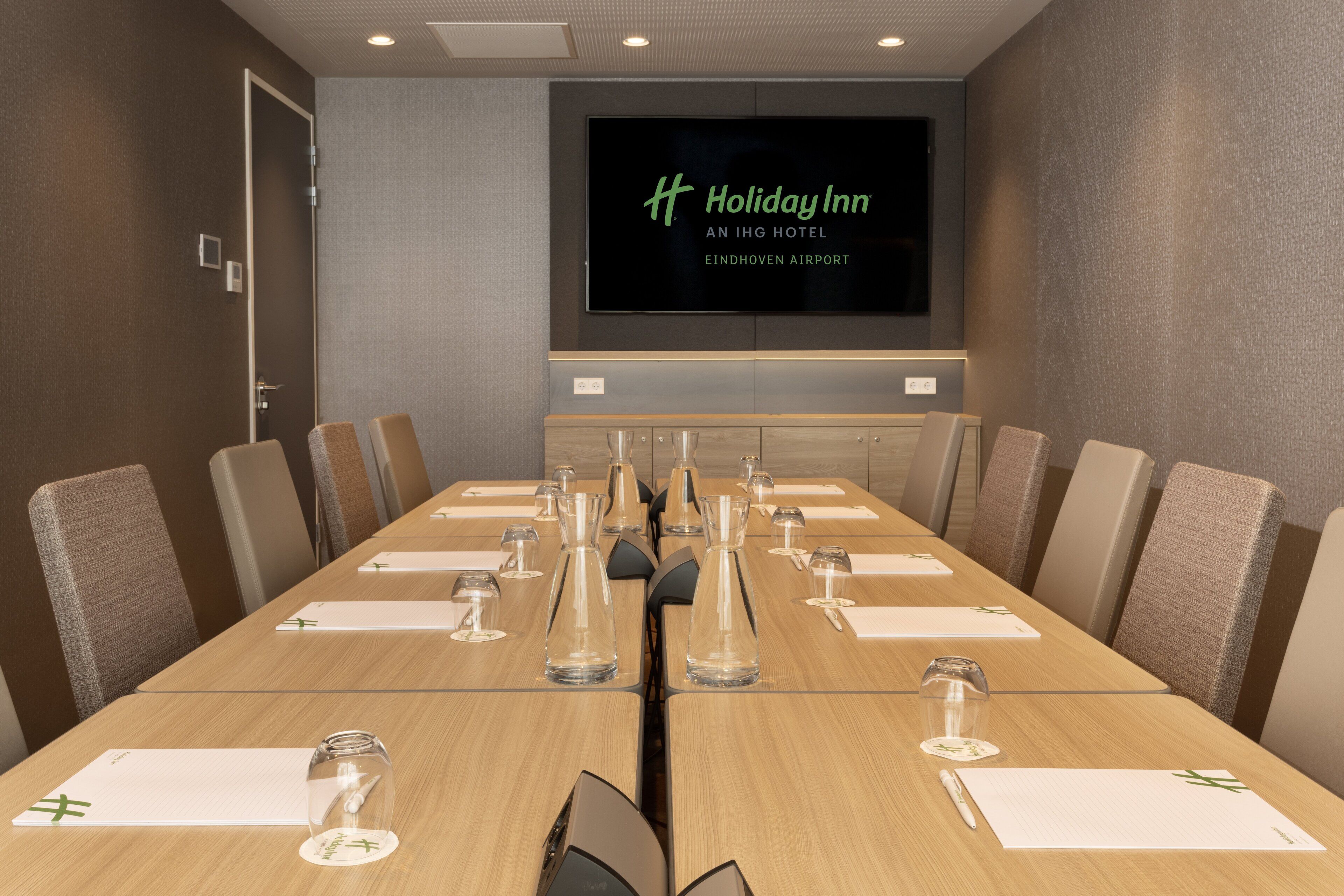 A conference room with a long table, chairs, and a screen displaying the Holiday Inn logo.