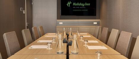 A conference room with a long table, chairs, and a screen displaying the Holiday Inn logo.