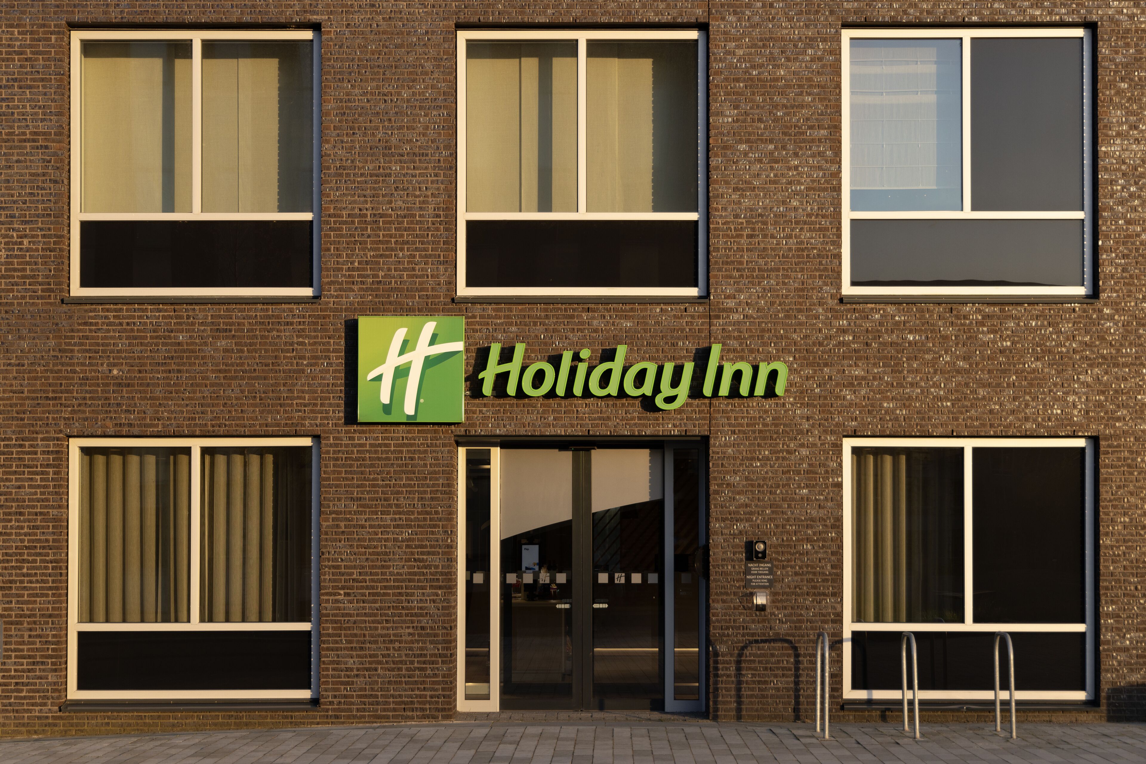 Un hôtel Holiday Inn avec une façade en briques, de grandes fenêtres et une enseigne verte.