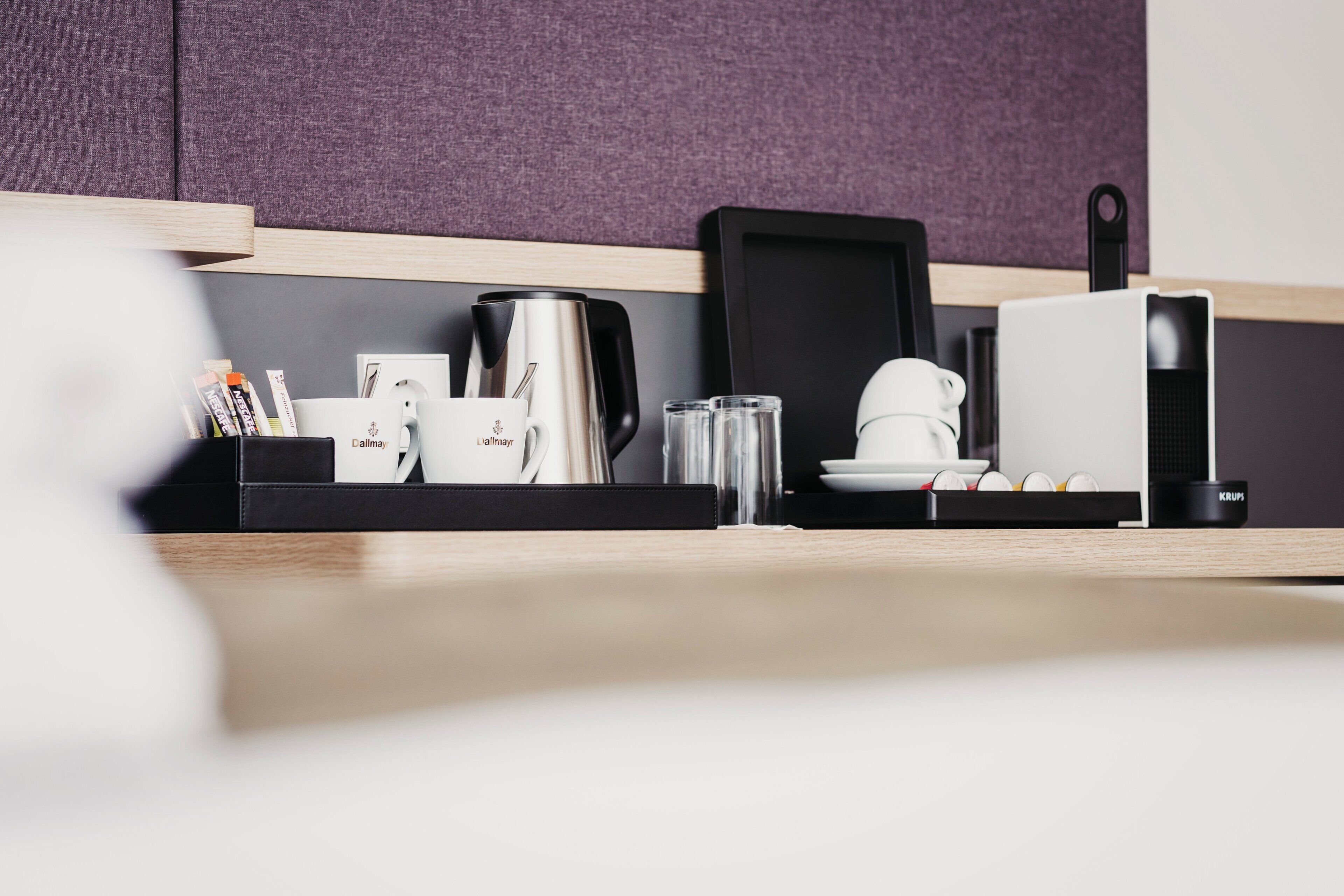 A modern kitchen with a coffee maker, mugs, a kettle, and a toaster on a black countertop.