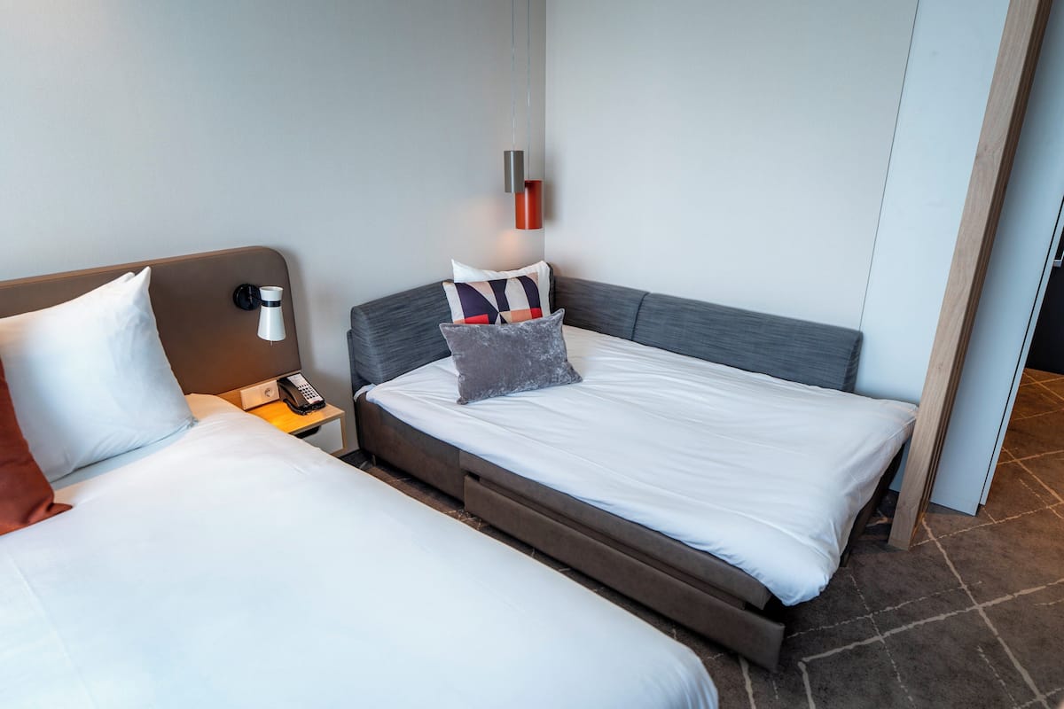A hotel room with two beds, a bedside table with a phone, and a wall-mounted light fixture.