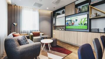 Ein modernes Wohnzimmer mit einer Couch, Sesseln, einem Couchtisch und einem an der Wand montierten Fernseher, der eine Holiday Inn Werbung zeigt.