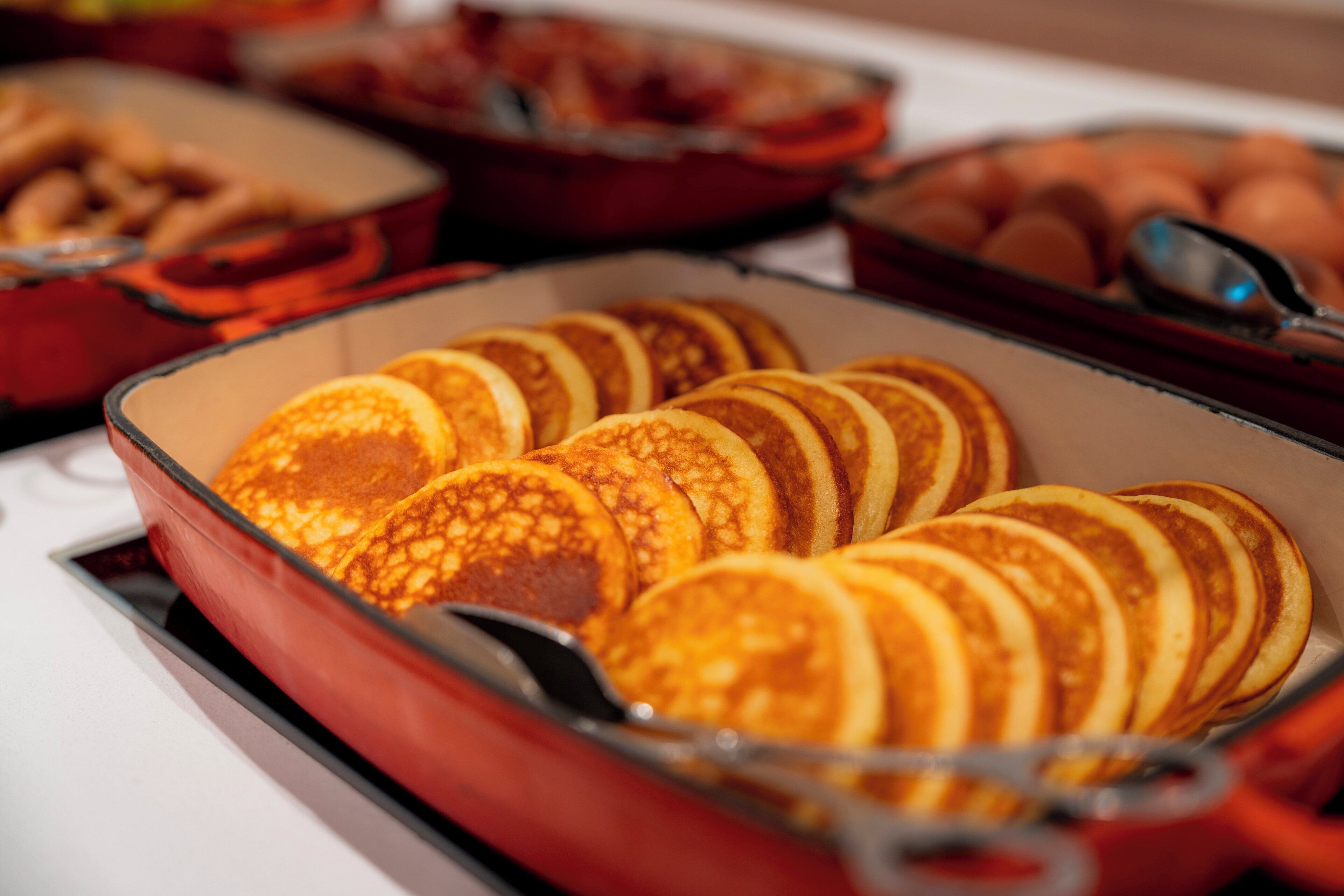 A breakfast buffet with various food items including pancakes, eggs, and pastries.