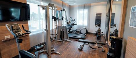 A gym with exercise equipment, a television, and large windows.