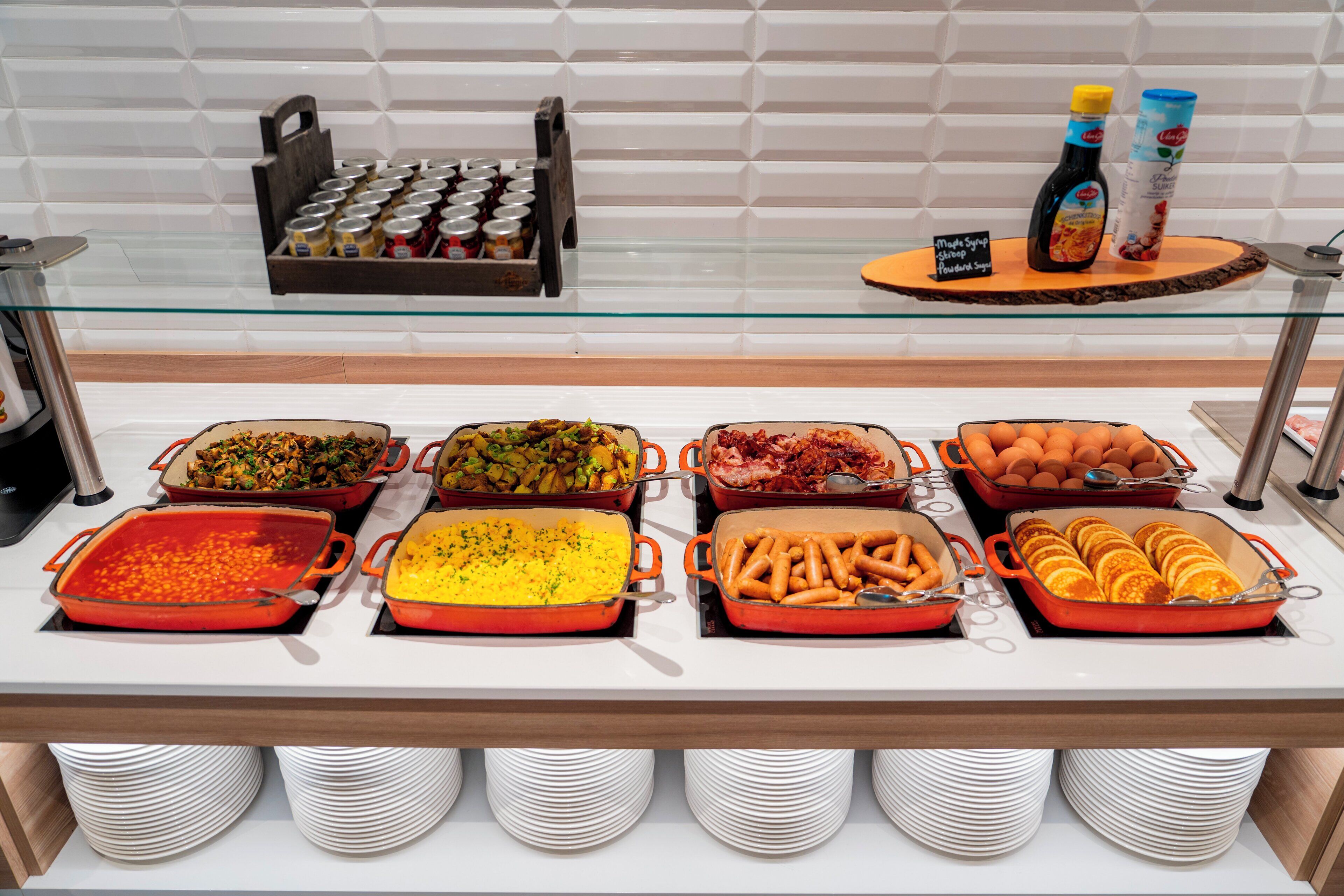 A buffet with various dishes in red and orange chafing dishes, including salads, rice, and meats.