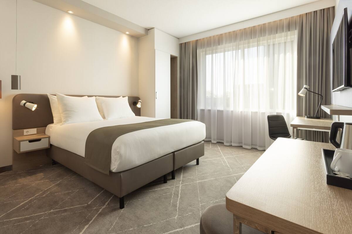 A modern hotel room with a large bed, a desk, and a TV.