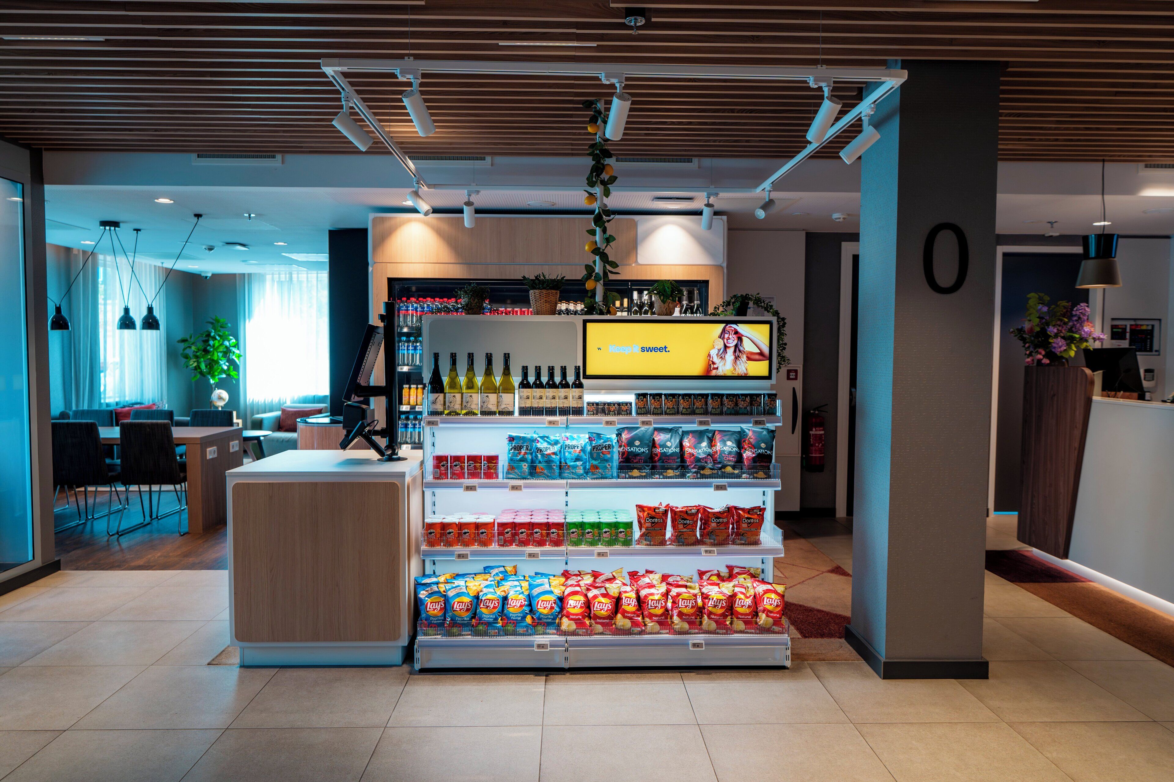 En modern butik med ett centralt placerat utbud av snacks och drycker, en digital informationsskylt och en ren och välordnad inredning.
