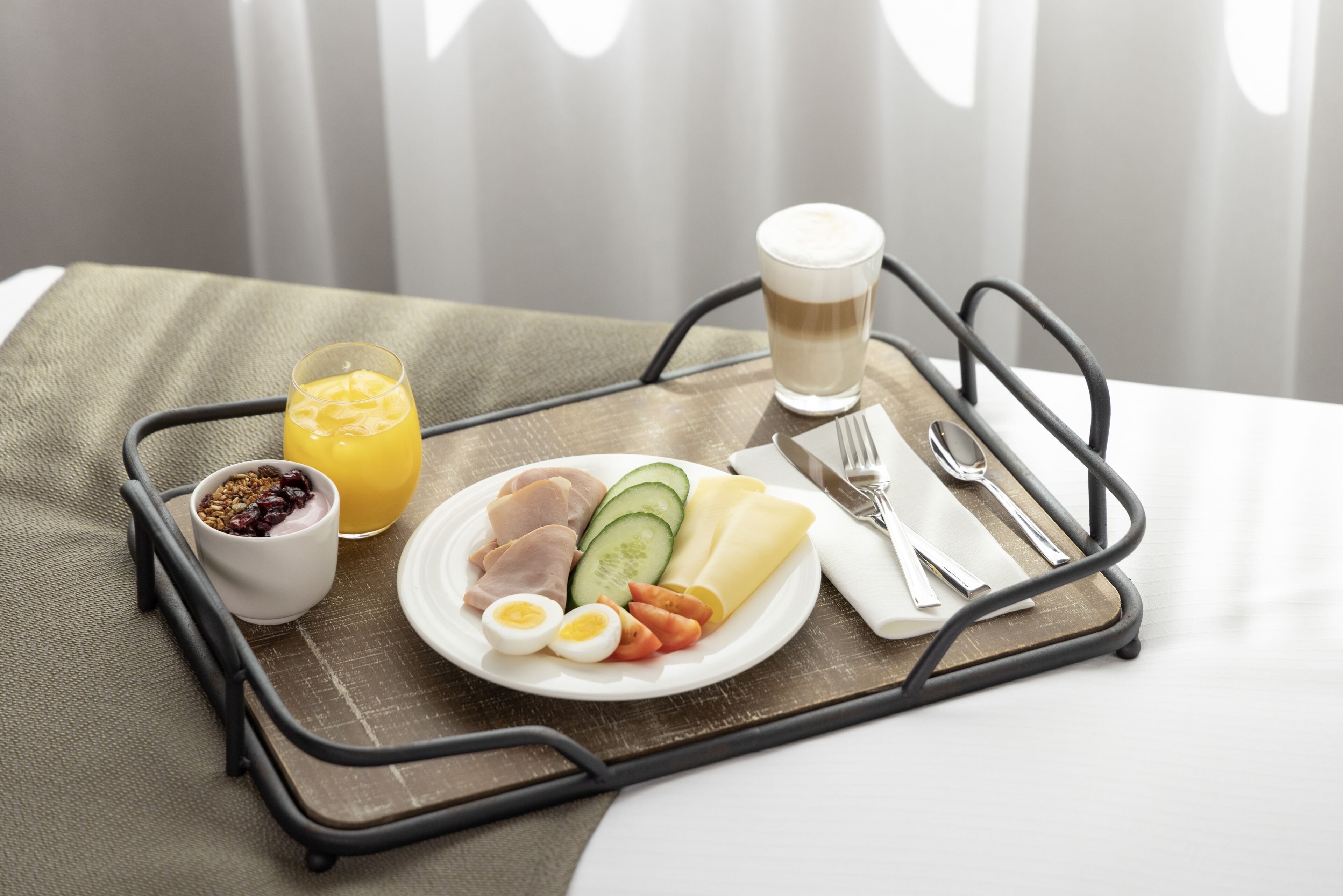Una bandeja de desayuno con un plato de comida, un vaso de jugo de naranja, una taza de café y un tazón pequeño de granola.