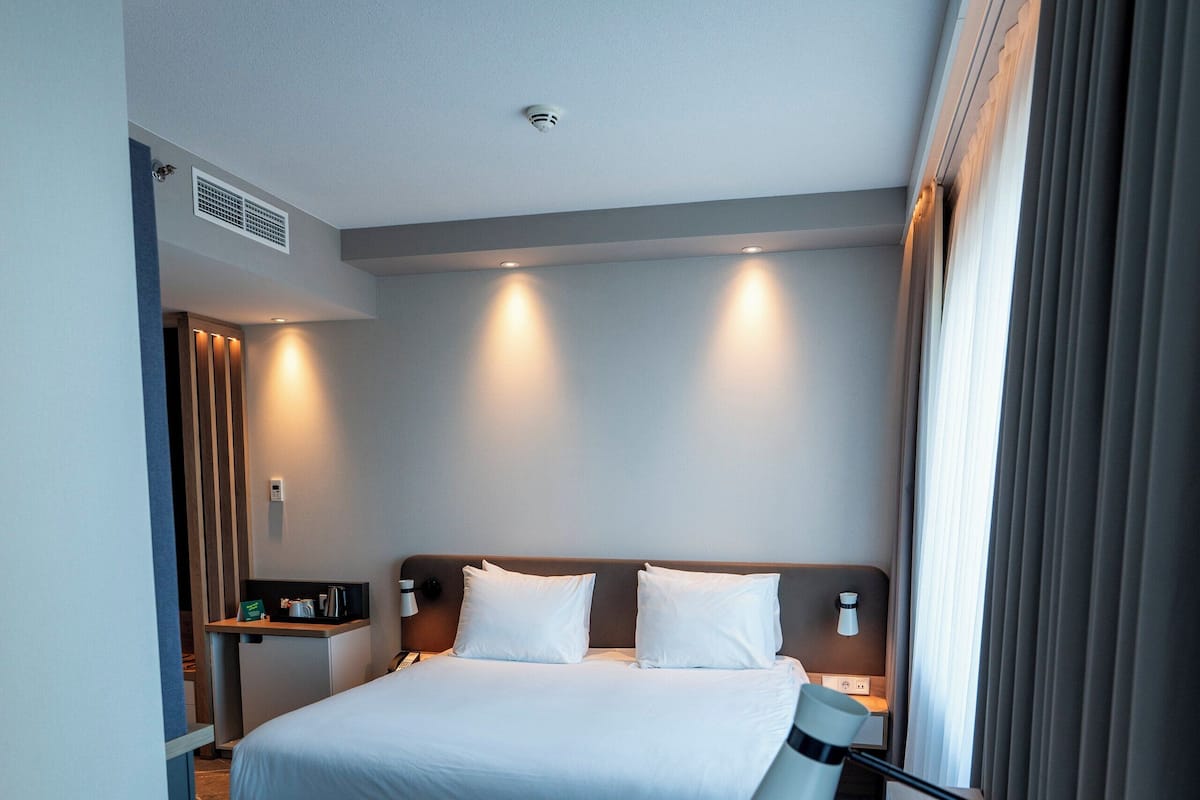 A hotel room with a large bed, bedside tables, a desk, a chair, and a window with curtains.