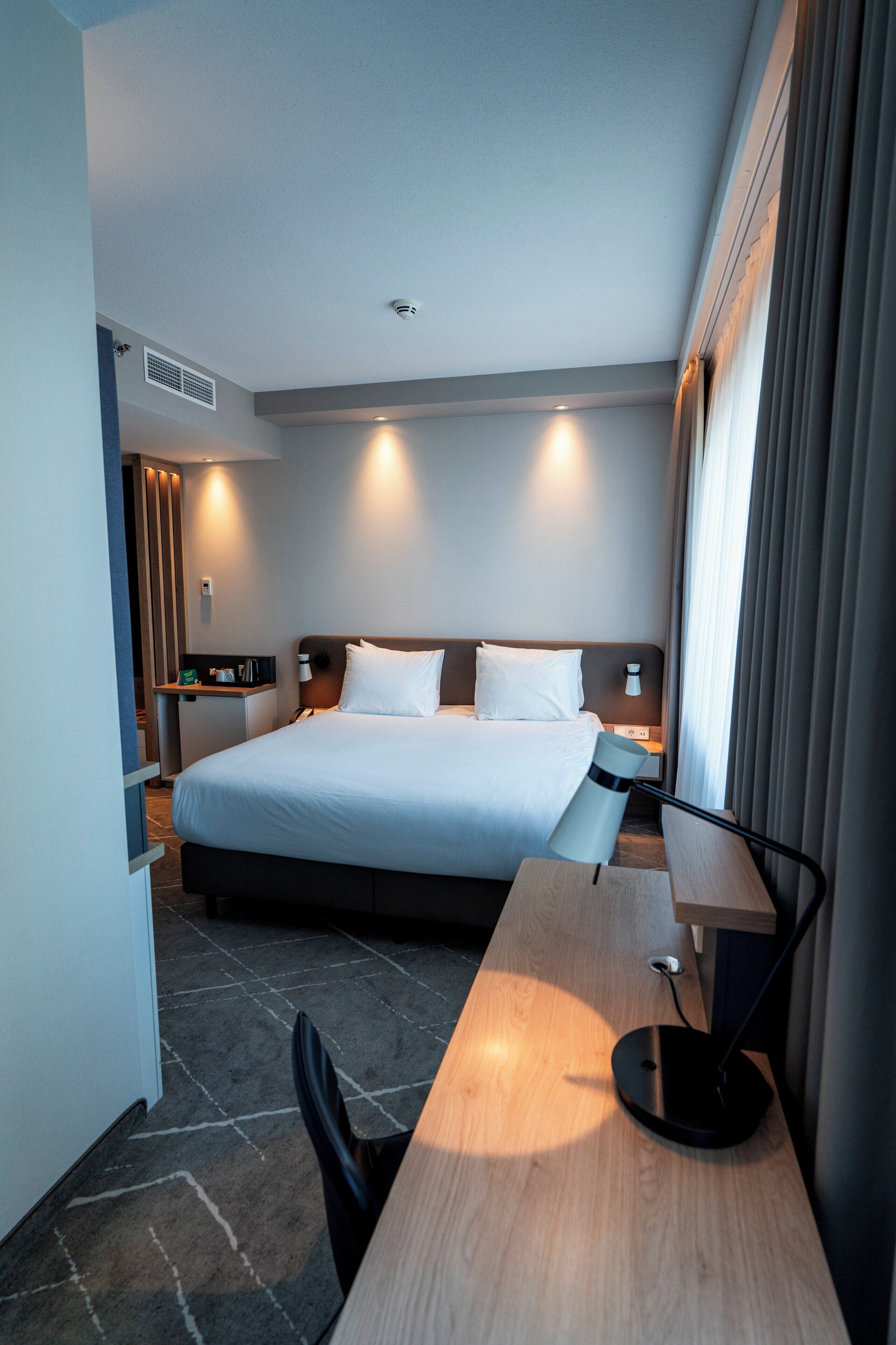 Una habitación de hotel moderna con una cama grande, mesitas de noche, un escritorio y una silla.