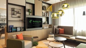 A modern hotel lobby with a flat-screen TV, comfortable seating, and decorative shelves. - Holiday Inn Eindhoven Airport by IHG (Eindhoven)