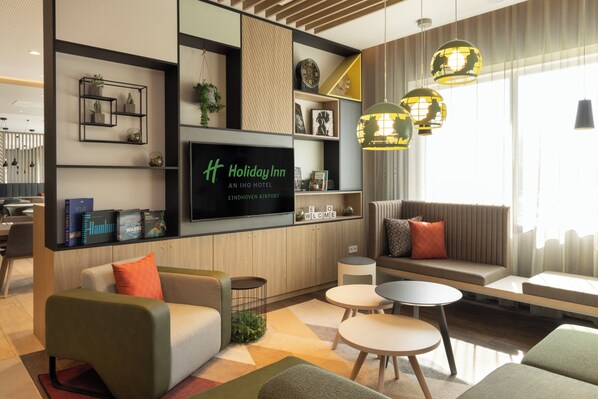 A modern hotel lobby with a flat-screen TV, comfortable seating, and decorative shelves.