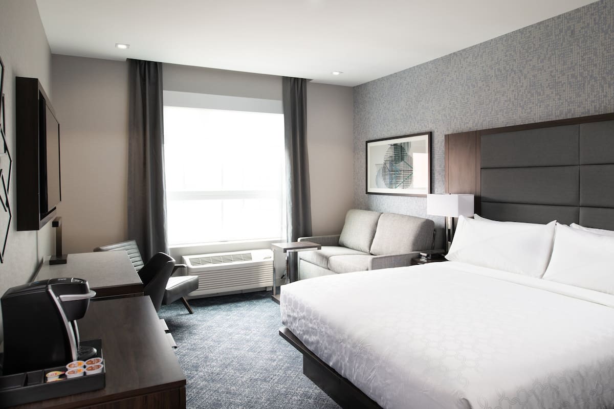 A hotel room with a large bed, a desk with a coffee maker, a sofa, and a TV.